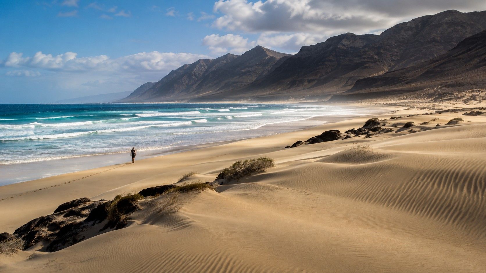 Breiter Sandstrand auf Fuerteventura mit Atlantikwellen